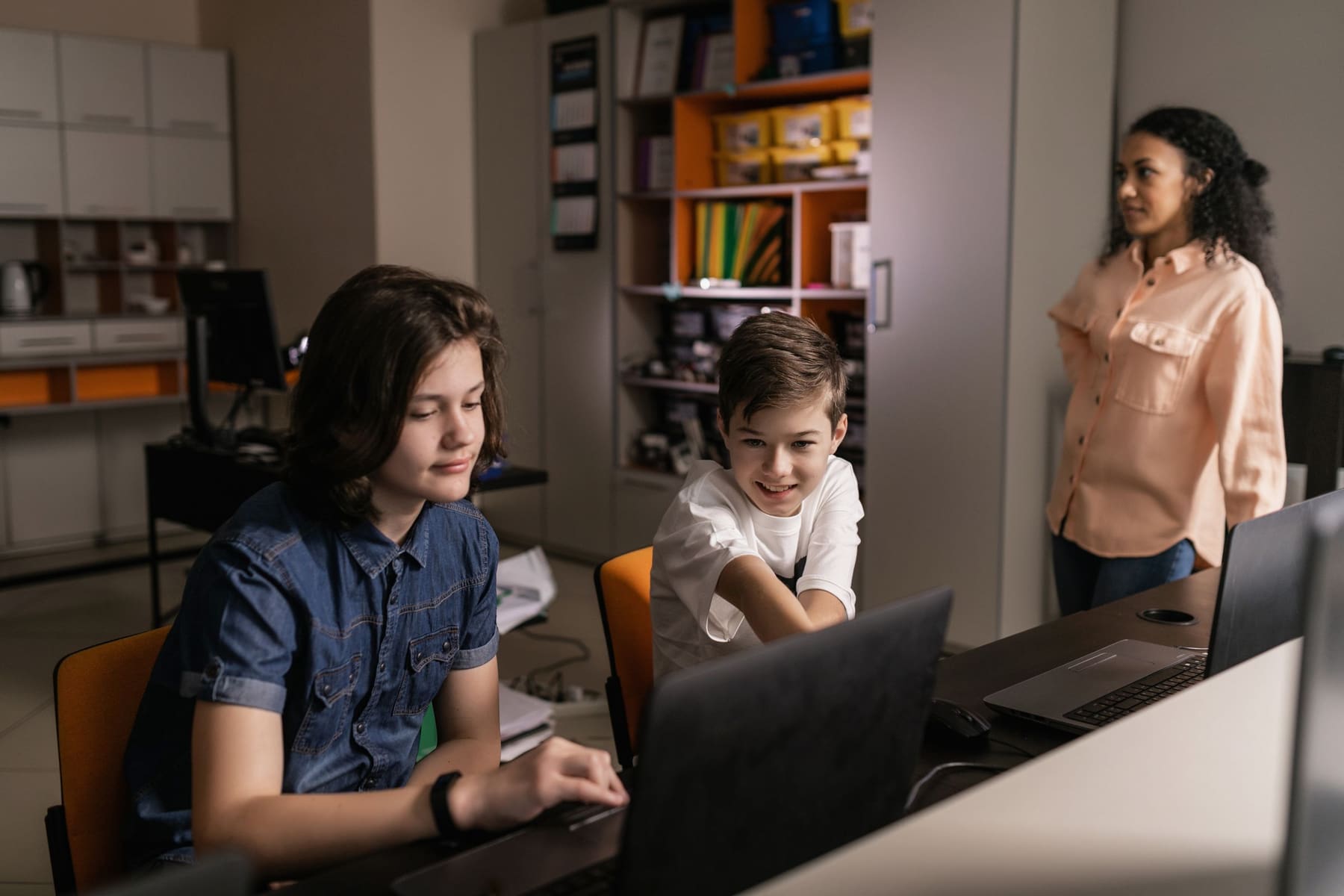 A teacher supervising students working on laptops