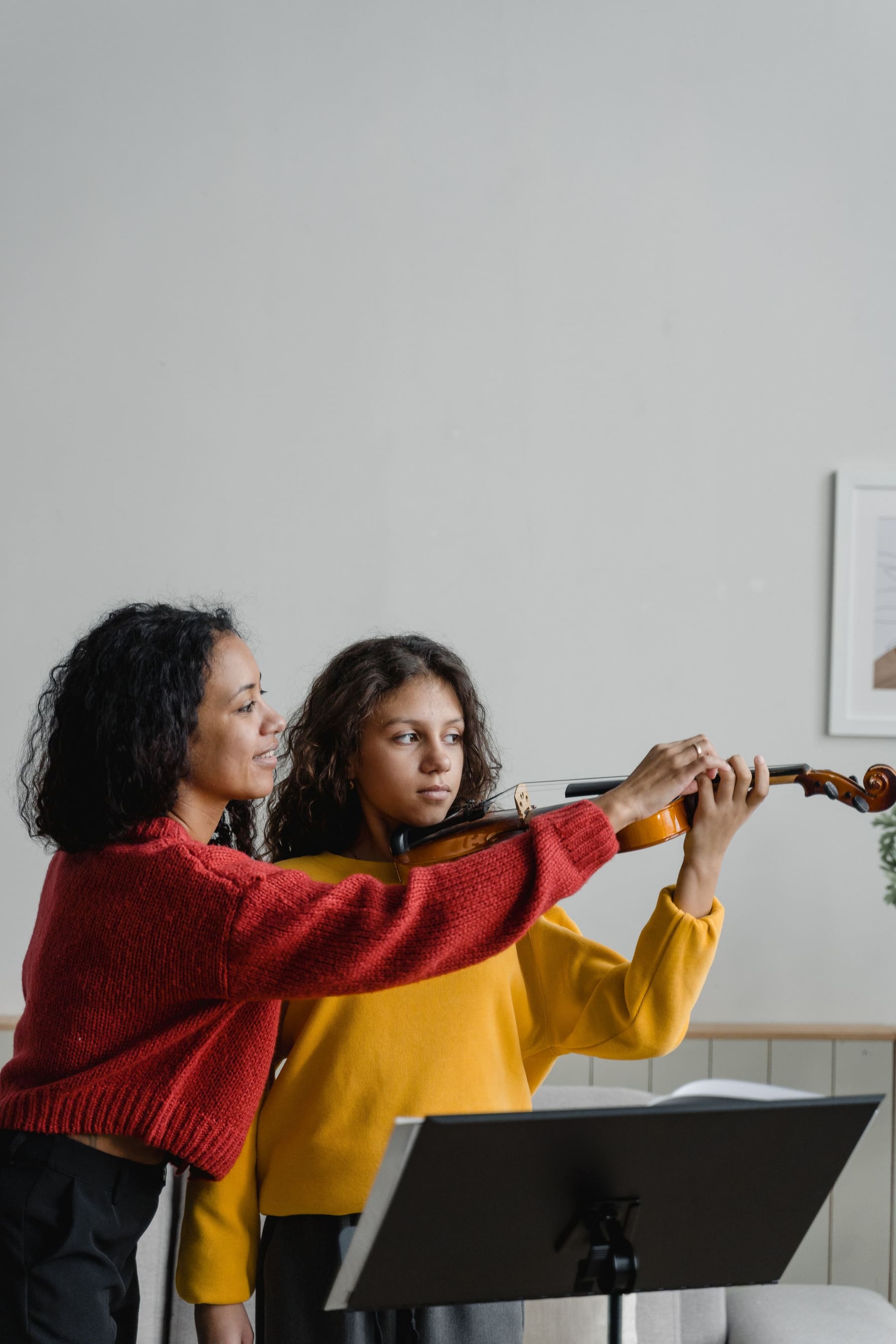 An adult guiding a girl as she learns to play the violin