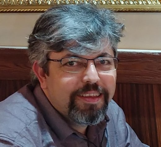 Ahmet Arduc, smiling, with glasses, grey hair and a beard